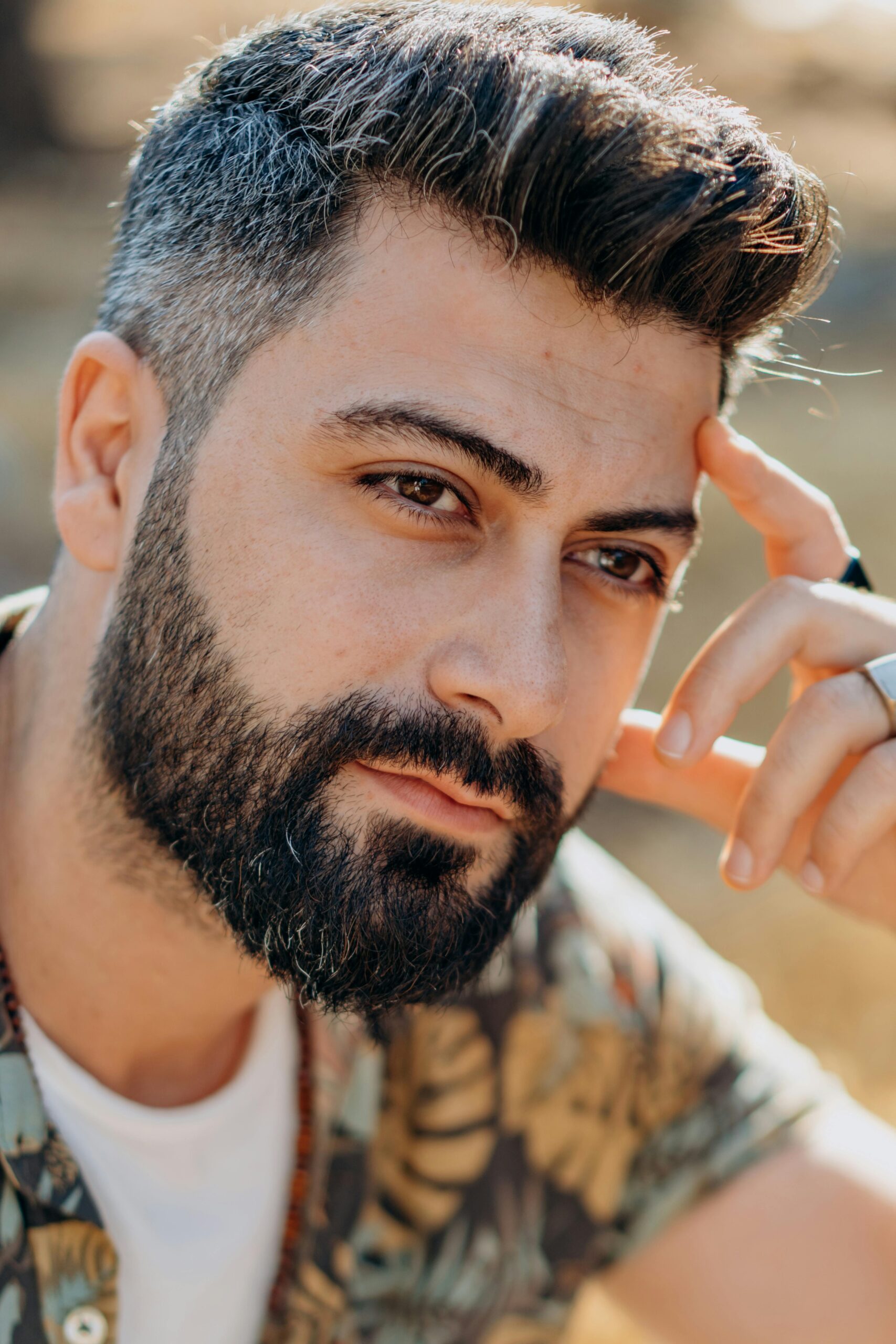 Portrait of a handsome bearded man with hand on head, captured in warm outdoor lighting, expressing deep thought.